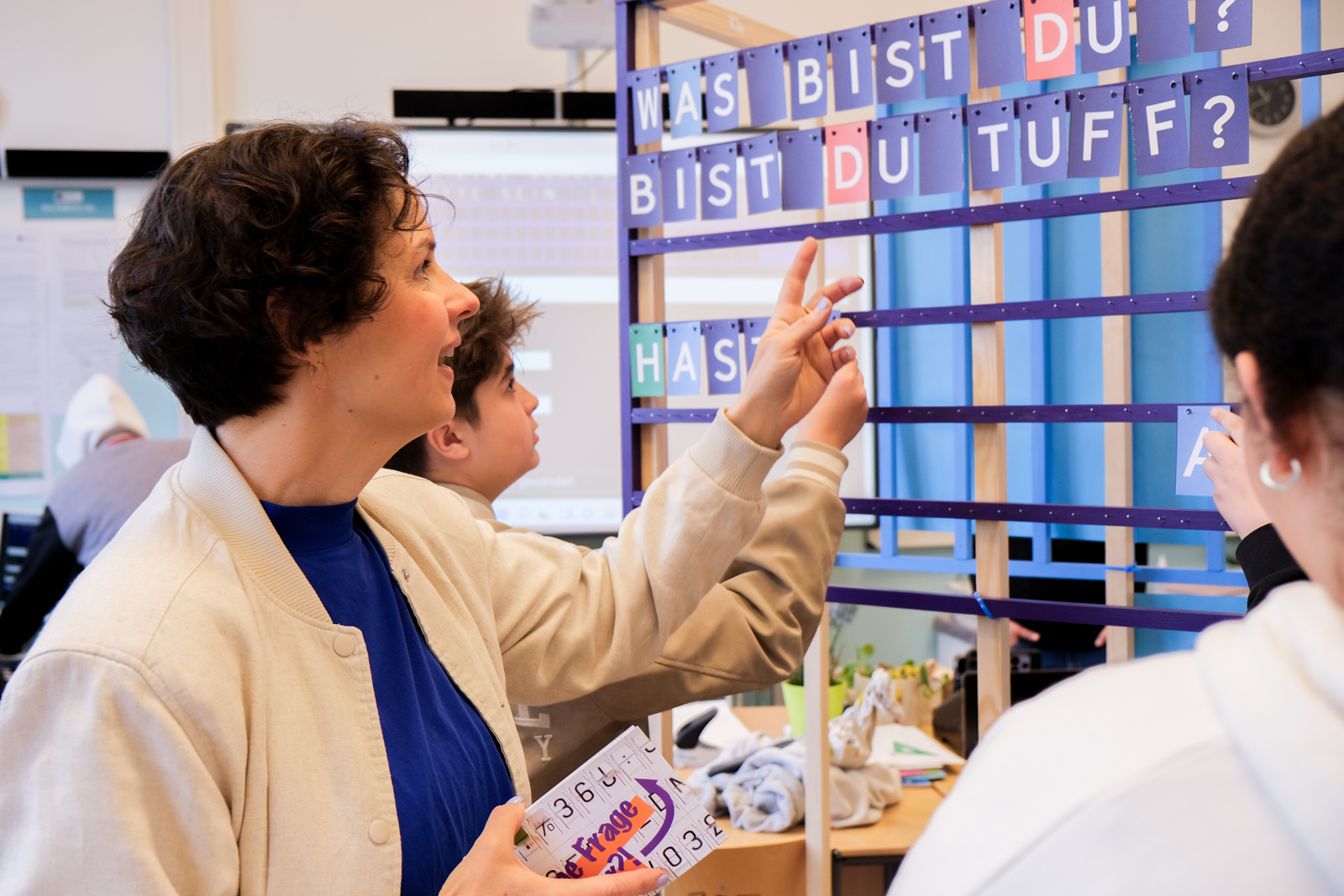 Künstlerin und Schülerinnen schauen auf Buchstaben an einem analogen Display